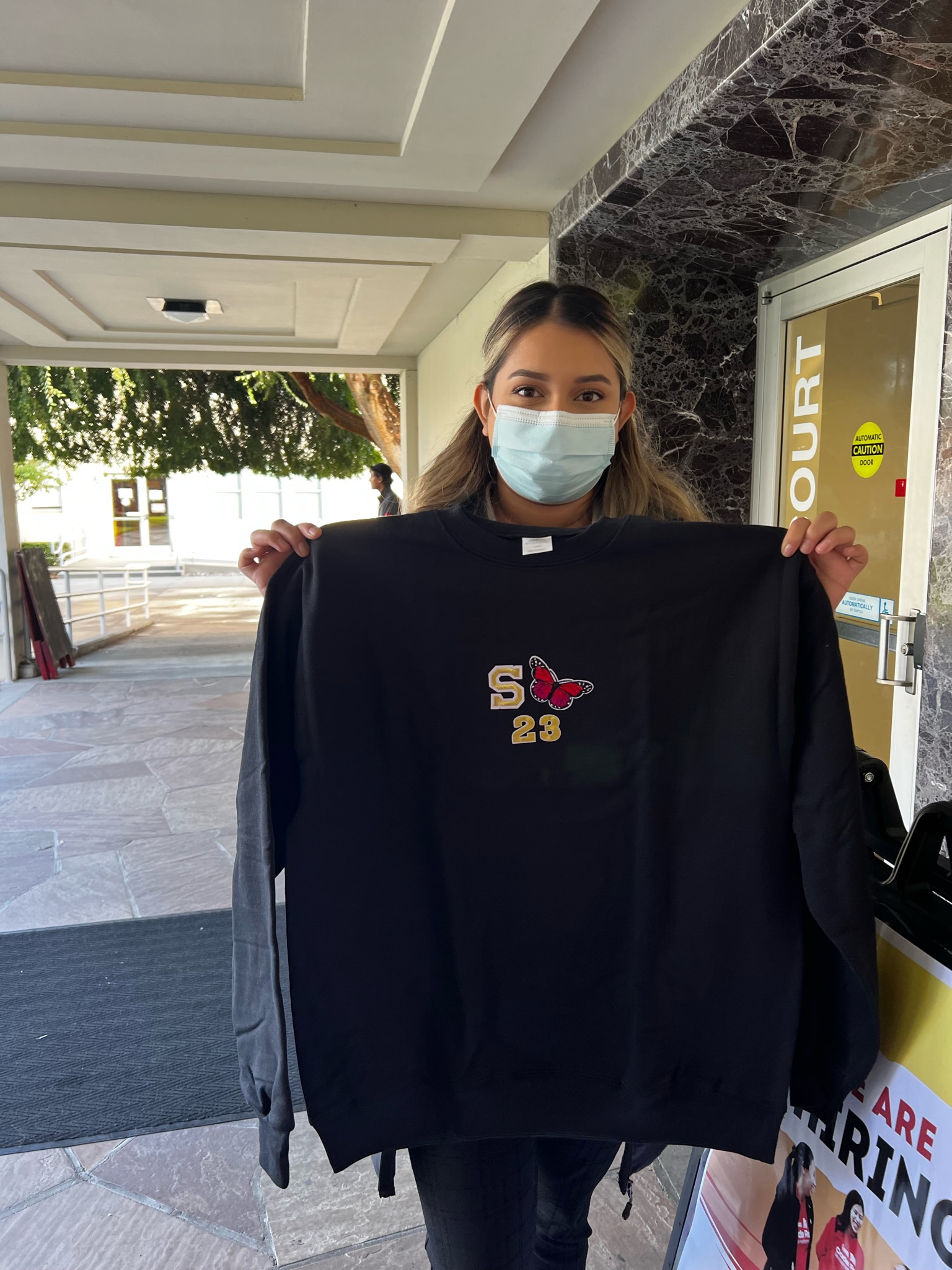 Stockton campus student holding up black Stan State sweatshirt that reads 'S (butterfly embroidered) 23'